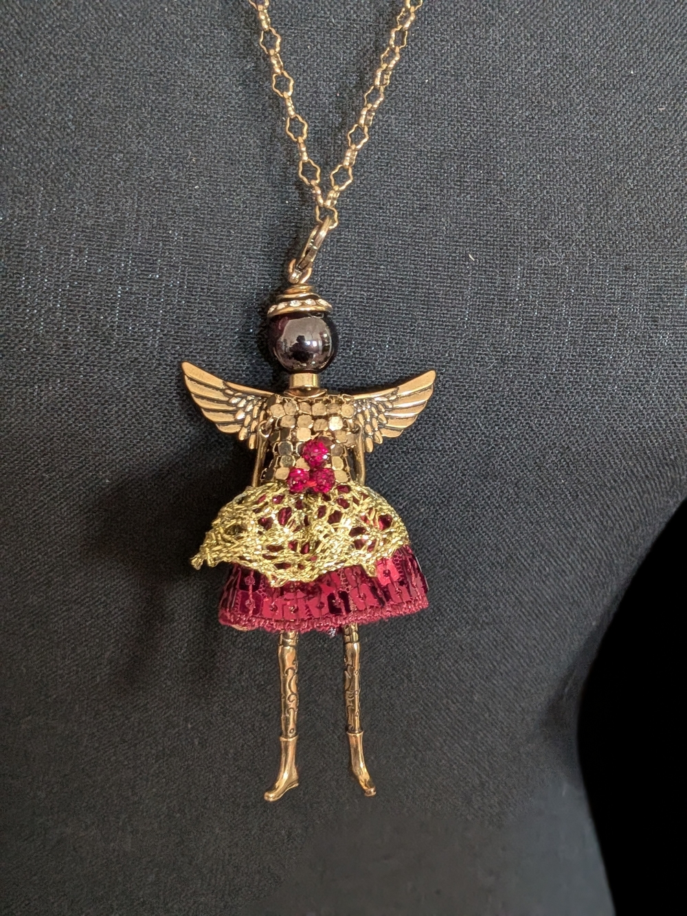 Jacqueline Kent angel necklace features a red gemstone-colored dress